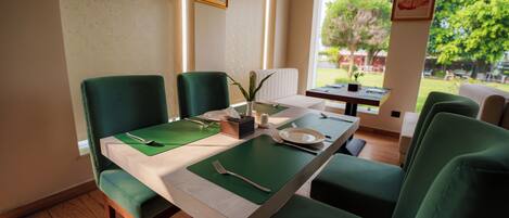Comedor con una mesa dispuesta para cuatro, sillas tapizadas en verde y ventana con vistas al follaje exterior.