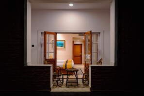 A hotel room with a bed, a small table, two chairs, a rug, and a painting on the wall. - Dreamland Gold Resort (Tilottama)