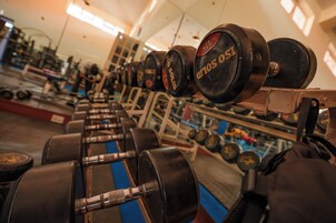 Una fila de equipo de levantamiento de pesas, incluyendo mancuernas y barras, en un gimnasio.