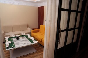 Una habitación con una mesa de comedor preparada para cuatro personas, un sofá, un sillón amarillo y una puerta con marco negro.