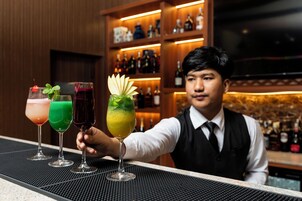 Un cantinero presenta tres bebidas en una barra, con estantes llenos de botellas al fondo.