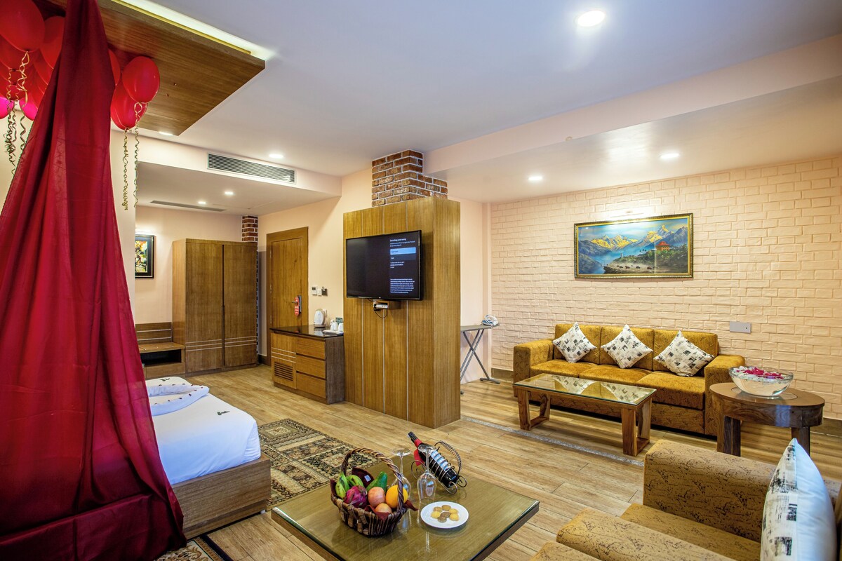 Une chambre d’hôtel avec un lit, une télévision, un canapé, une table basse et un tableau au mur.