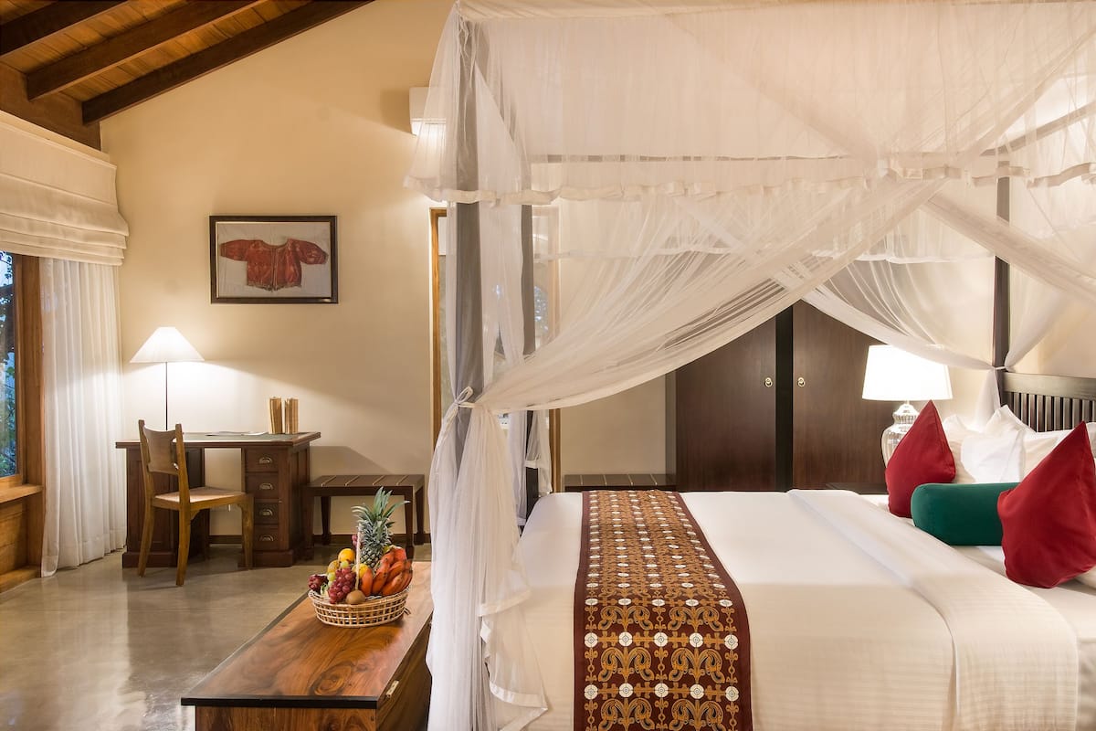 A bedroom with a canopy bed, a desk with a chair, and a fruit basket on the nightstand.