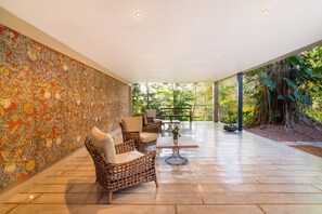 A covered patio with wicker furniture, a tiled floor, and a mural on the wall.