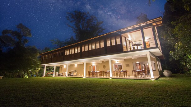 A two-story house with a covered patio and a dining area, surrounded by a well-maintained lawn and trees. - Kings Pavilion (Kandy)
