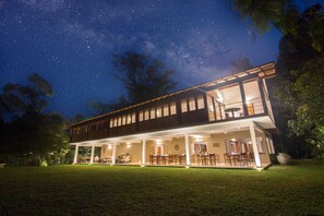 A two-story house with a covered patio and a dining area, surrounded by a well-maintained lawn and trees. - Kings Pavilion (Kandy)