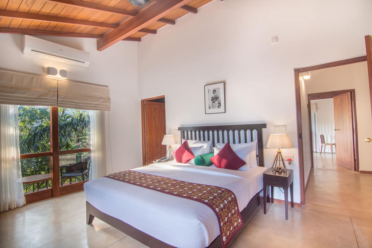 A bedroom with a large bed, a nightstand, a window with curtains, and a door leading to another room.
