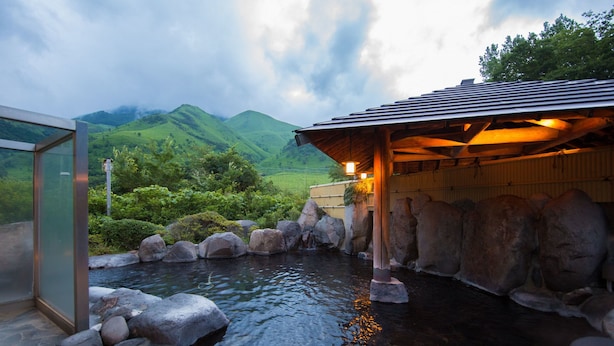 A traditional Japanese onsen with a wooden structure, a rock-lined pond, and a view of green hills in the background. - Yufuin Onsen Yufuin Nanairo No Kaze (Yufu)