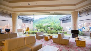 A spacious living area with sofas, a coffee table, and a TV. Large windows offer a view of a garden and mountains. - Yufuin Onsen Yufuin Nanairo No Kaze (Yufu)