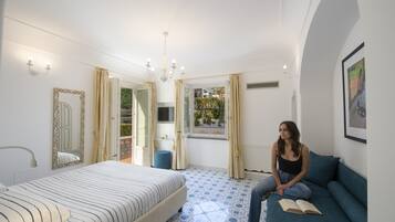 Un dormitorio con una cama, un sofá azul, un ventanal grande y una puerta que da a un balcón.