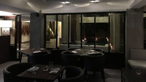 Un comedor moderno con un separador de vidrio, mobiliario en tonos oscuros e iluminación empotrada en el techo.