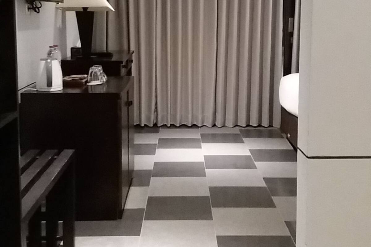 A hotel room with a checkered floor, a desk with a lamp, a television, and a bathroom with a sink and toilet.