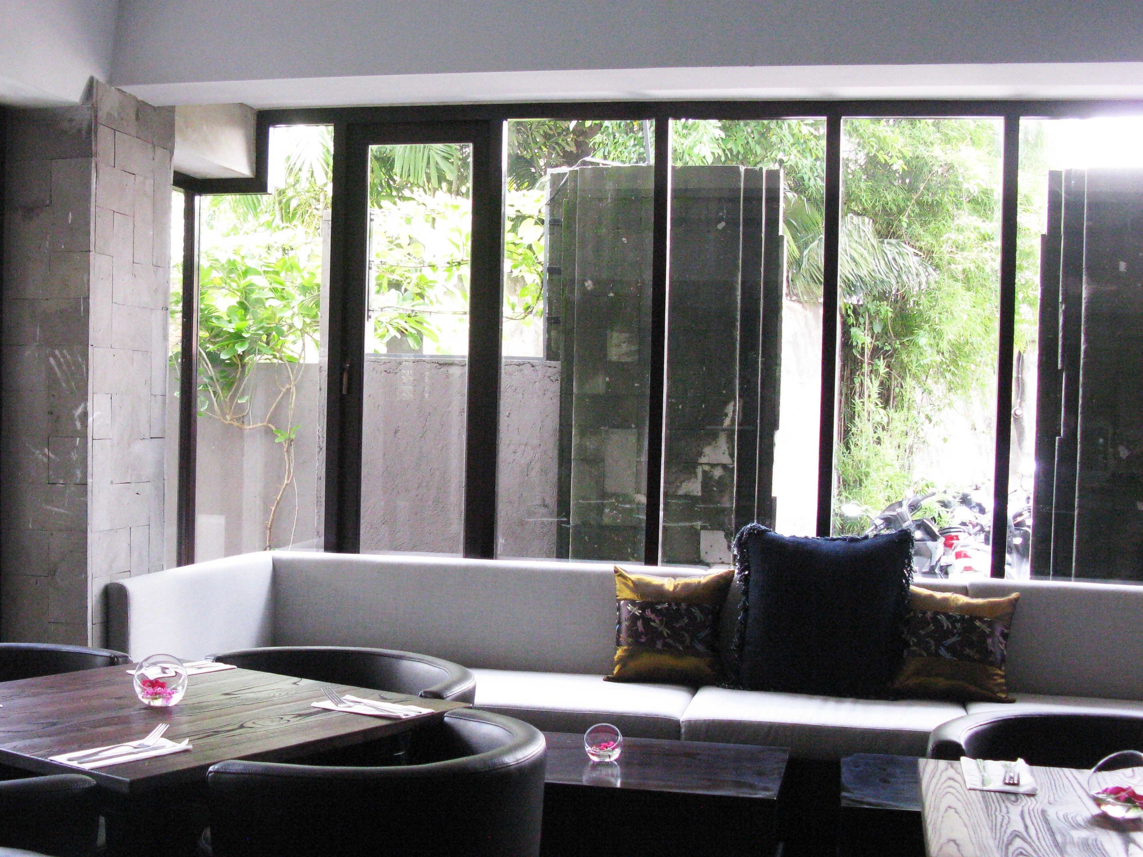A room with a white sofa, a dining table with a glass bowl and cutlery, and a window with a view of greenery outside.
