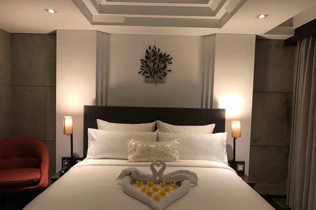 A hotel room with a large bed, two bedside lamps, a red chair, and a decorative wall piece.