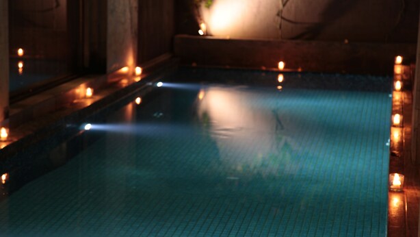 Un área de piscina interior tenuemente iluminada, con suelo de baldosas y pequeñas velas a lo largo de los bordes.