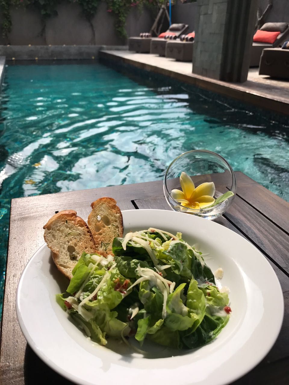 A dining table with a plate of food and a glass of water by a pool.