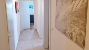 Un couloir aux murs blancs, au sol carrelé, et orné d’un grand tableau représentant un paysage montagneux.