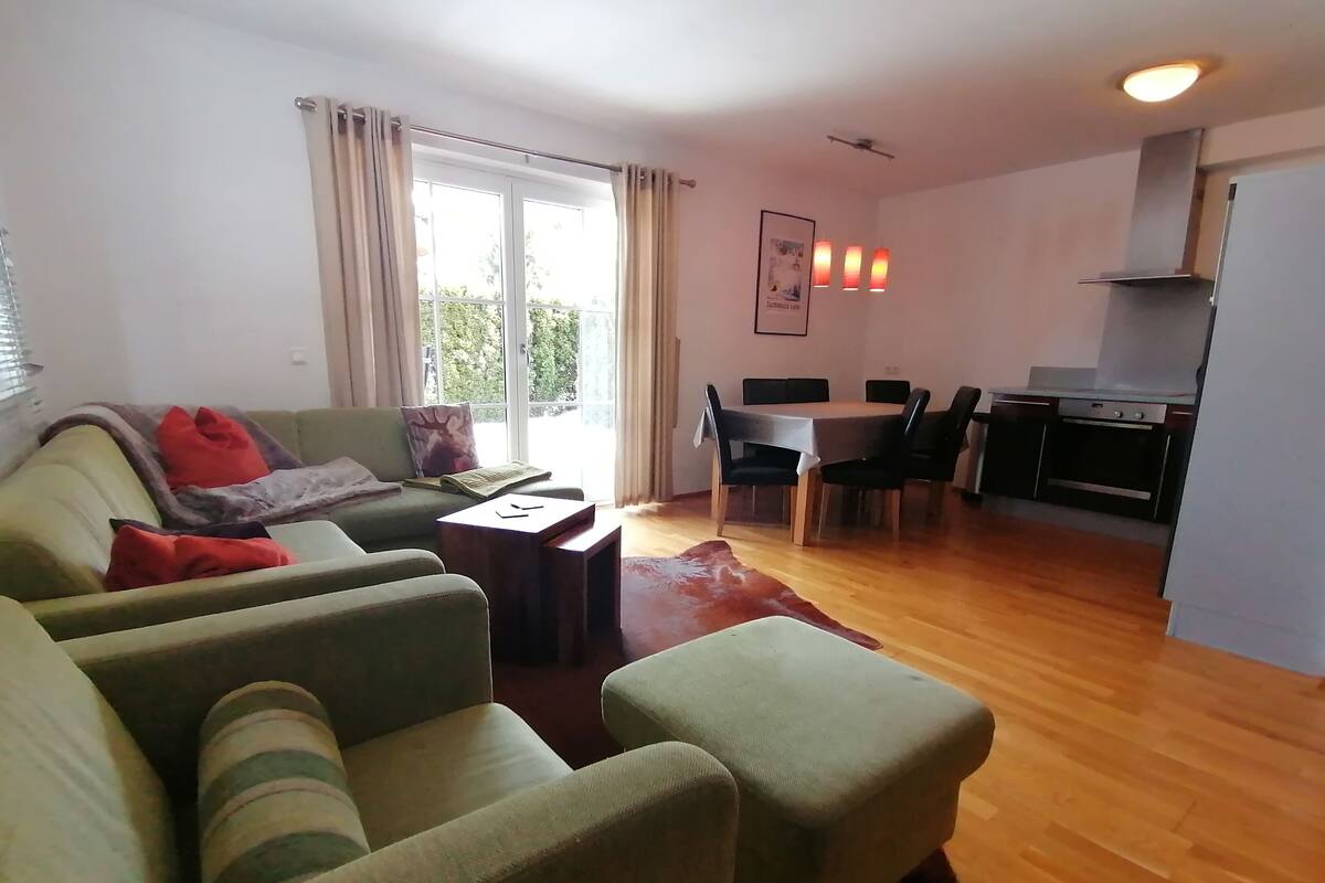 Una sala de estar con sofá, reposapiés y una zona de comedor con mesa y sillas.