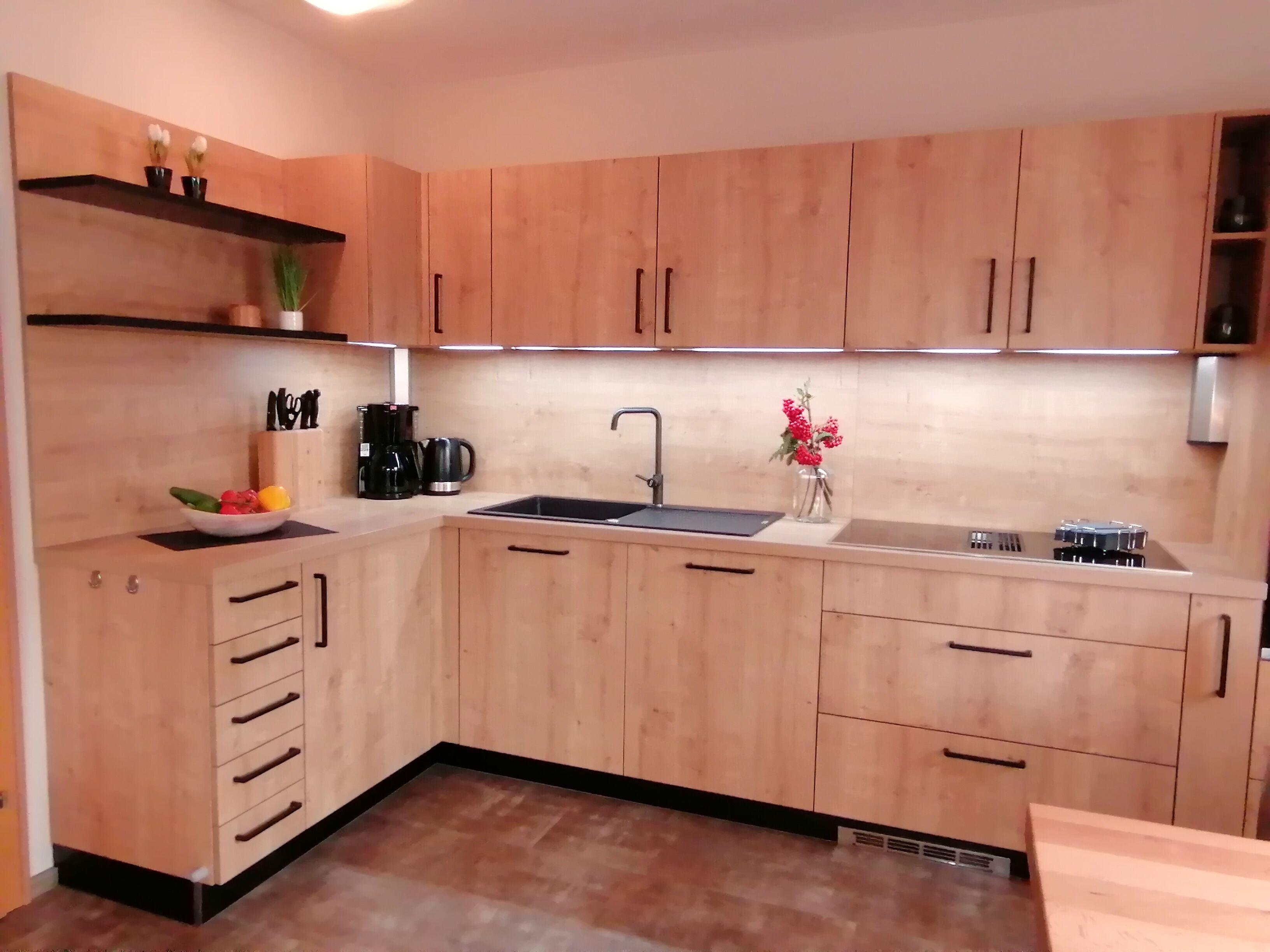 Una cucina moderna con mobili in legno, un piano di lavoro nero, un lavello e una macchina da caffè.
