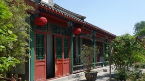 Un edificio tradicional con puertas rojas y marcos de ventana verdes, techo de tejas y una planta en maceta al frente.
