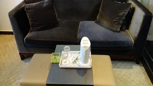 Un sofá azul oscuro con dos cojines oscuros, una mesita con una bandeja que sostiene un objeto blanco, y un objeto verde sobre la mesa.