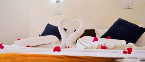 A neatly made bed with white and blue linens, a heart-shaped towel arrangement, and a framed artwork on the wall.