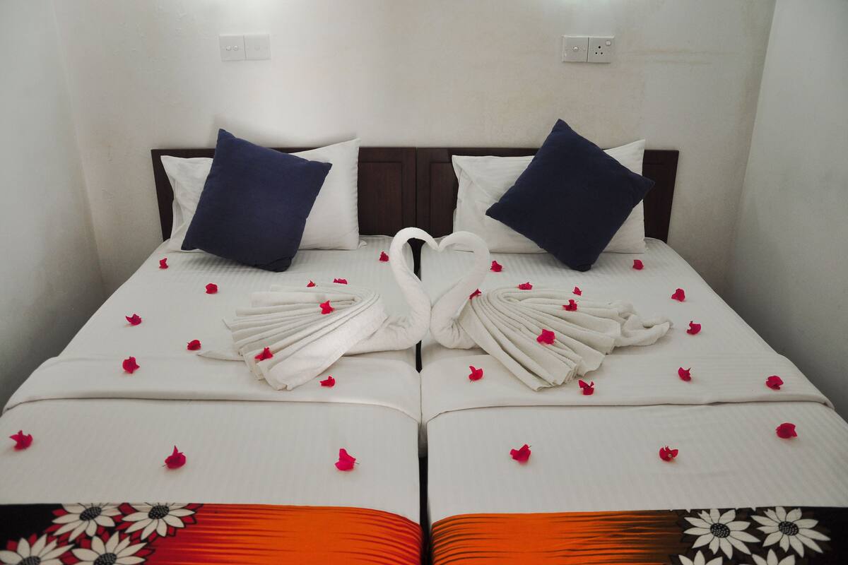 A neatly made bed with a heart-shaped towel arrangement and scattered rose petals.