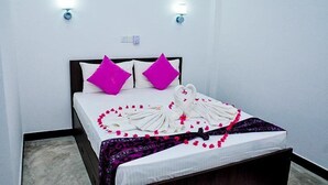 A neatly made bed with white linens, two bright pink pillows, and a decorative swan towel arrangement on the bedspread. - Sea Breeze (Mirissa)