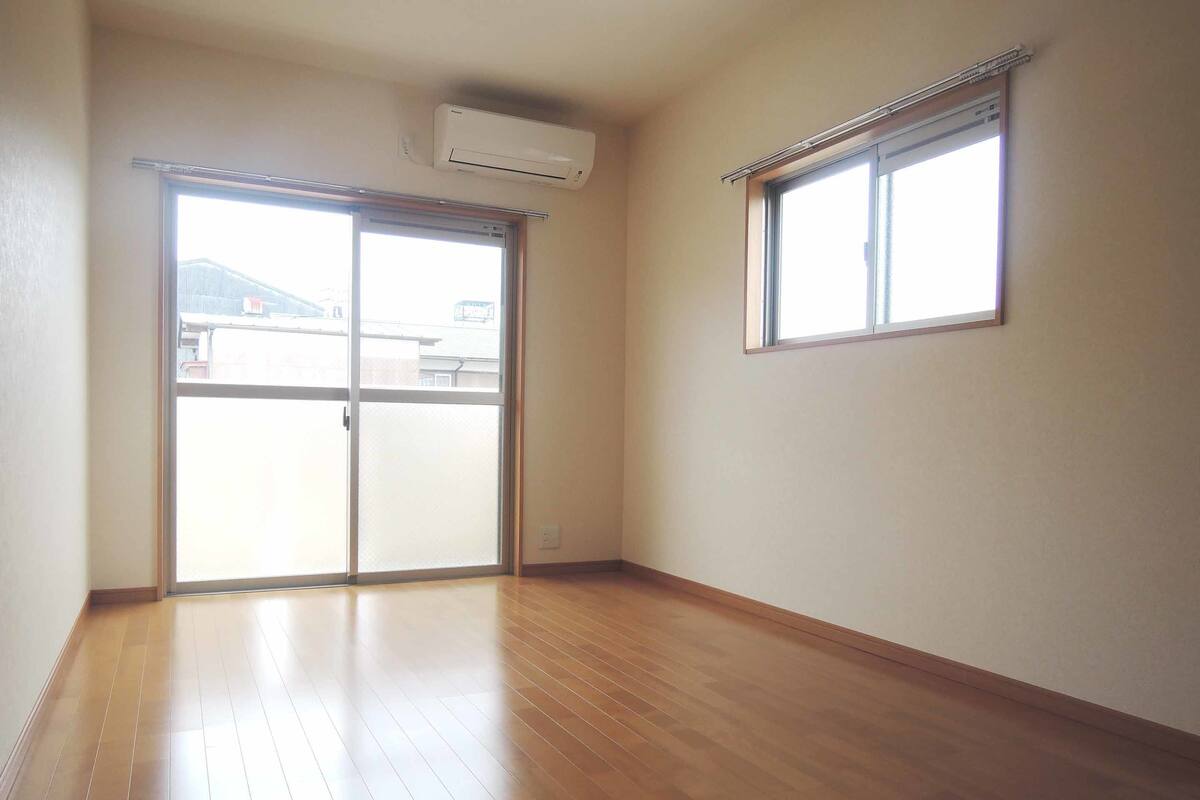A room with wooden flooring, a sliding glass door, a window, and an air conditioning unit.