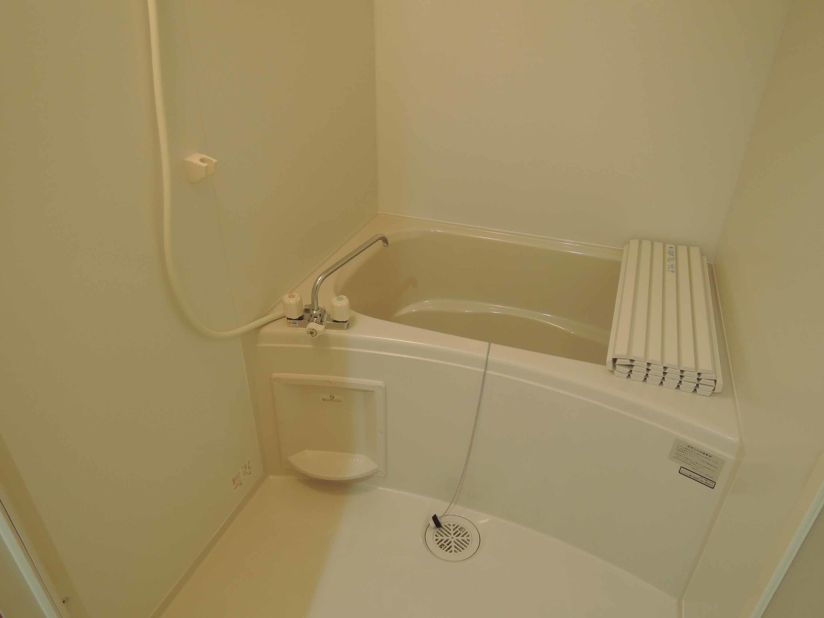 A small, white bathroom with a bathtub, a showerhead, and a towel rack.