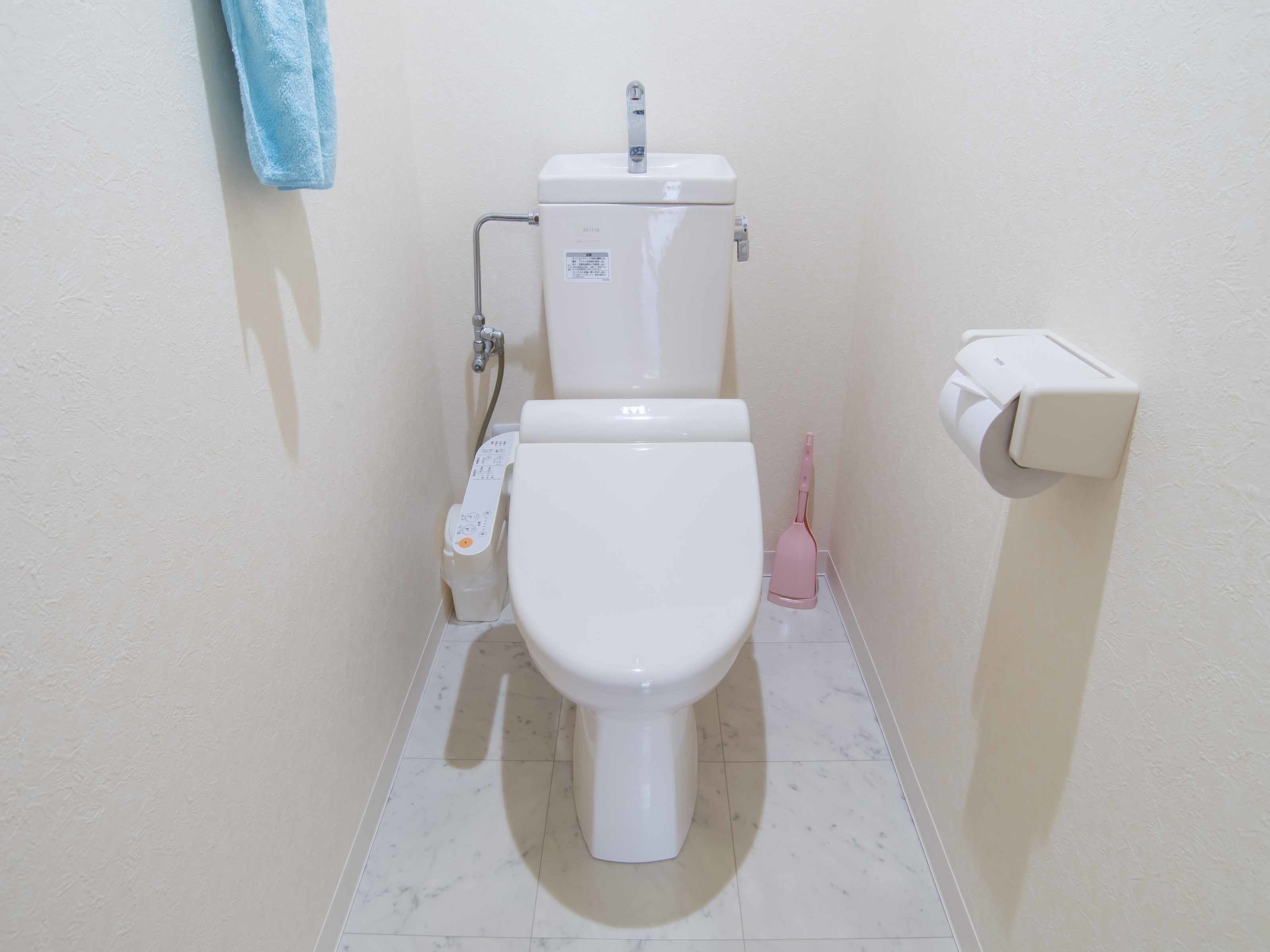 A standard toilet with a bidet attachment, a toilet paper holder, and a hand dryer.