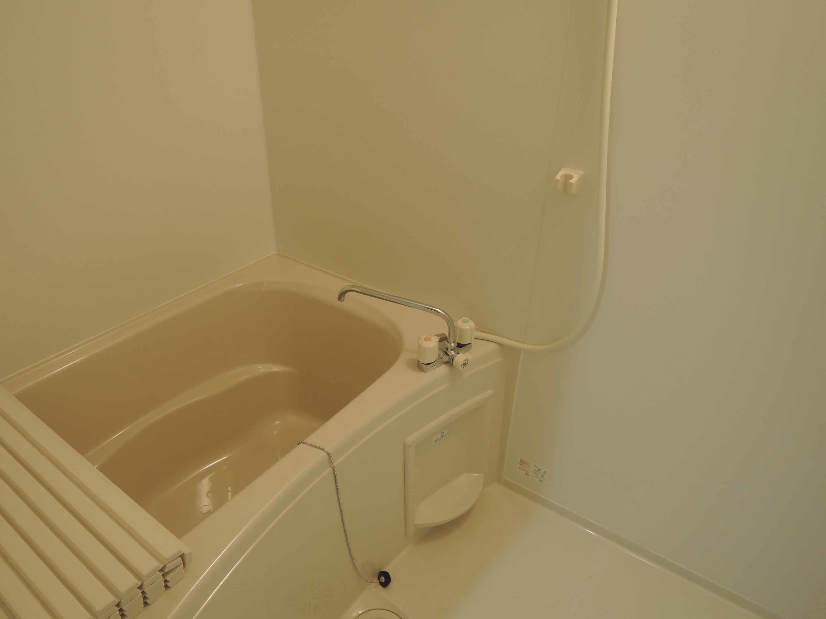 Una bañera estándar con ducha, un estante empotrado pequeño y un perchero de pared.
