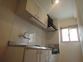 Una cocina compacta con armarios blancos, un lavamanos de acero inoxidable y una estufa empotrada.