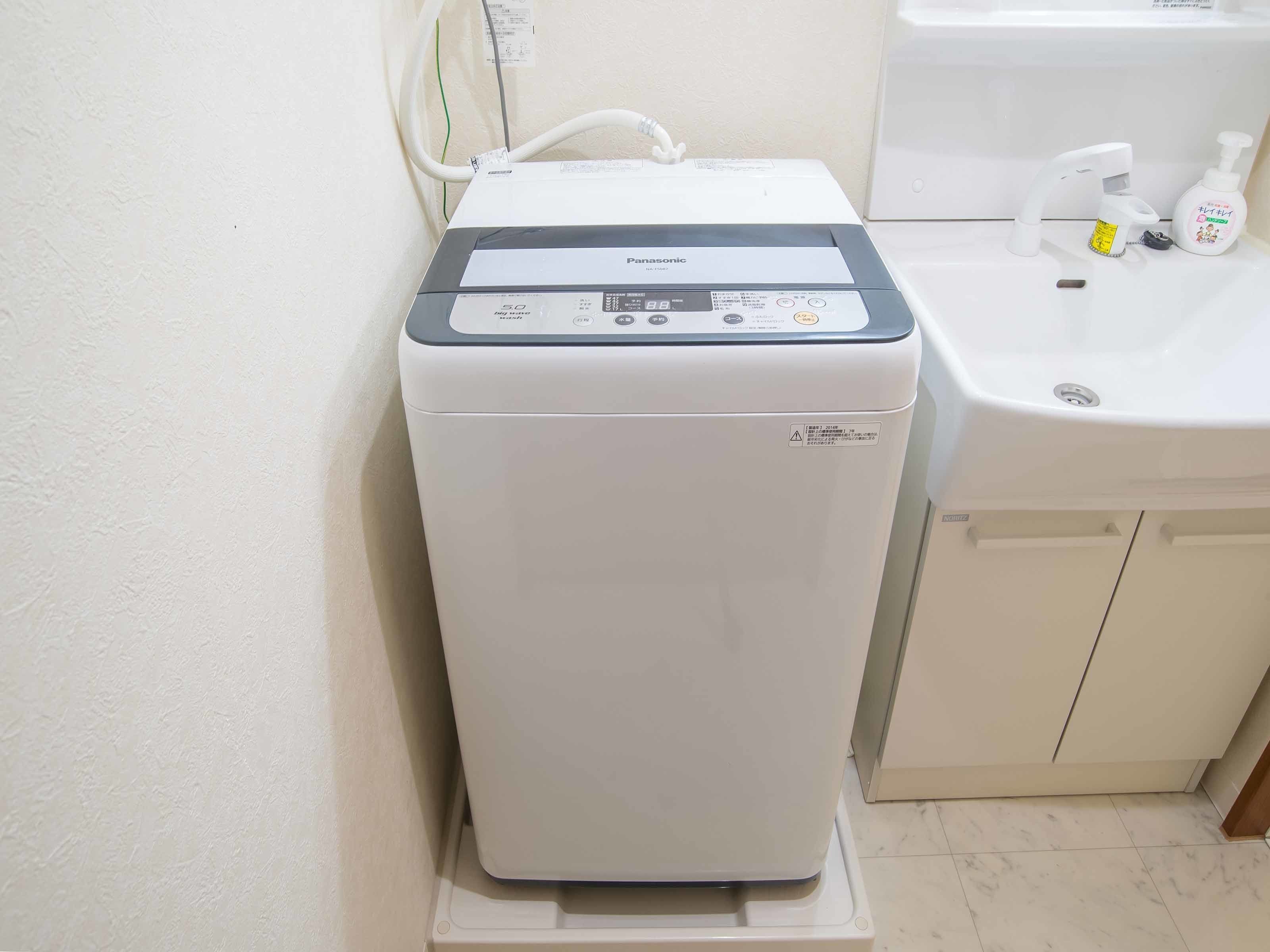 A compact, white Panasonic washing machine with a control panel, situated next to a sink with a soap dispenser.