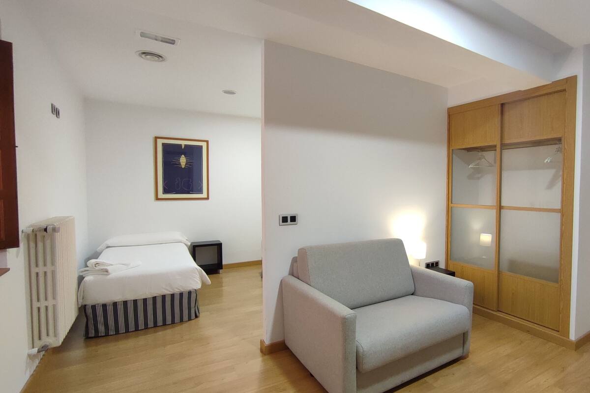 A hotel room with a bed, a chair, a wardrobe, and a radiator.