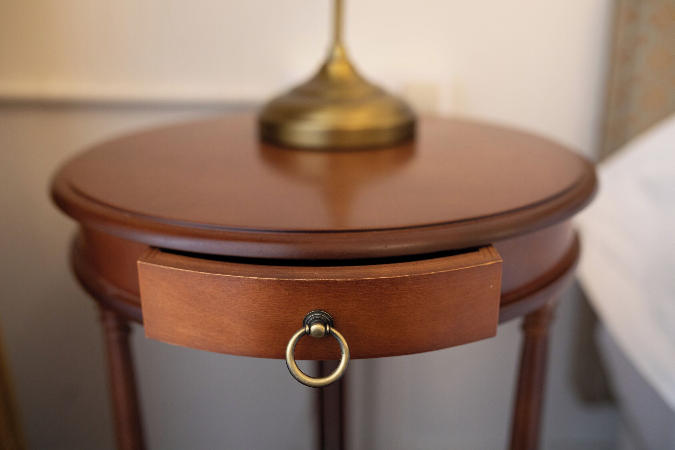A wooden bedside table with a brass lamp and a drawer with a ring pull.