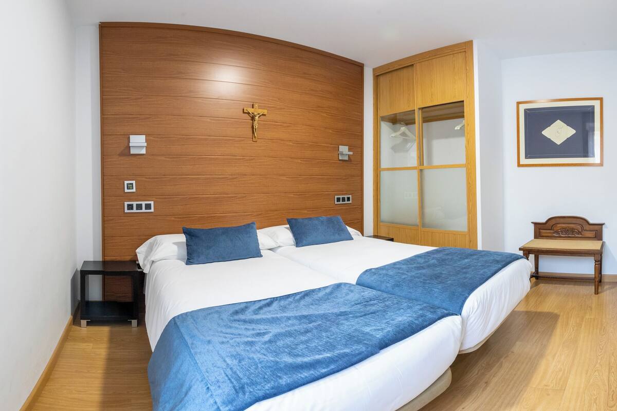 A double bed with a wooden headboard, a nightstand, a wooden wardrobe, and a framed picture on the wall.