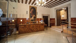 A reception area with a wooden counter, a chandelier, and a staircase leading to an upper level. - Hospedería del Seminario (Cuenca)