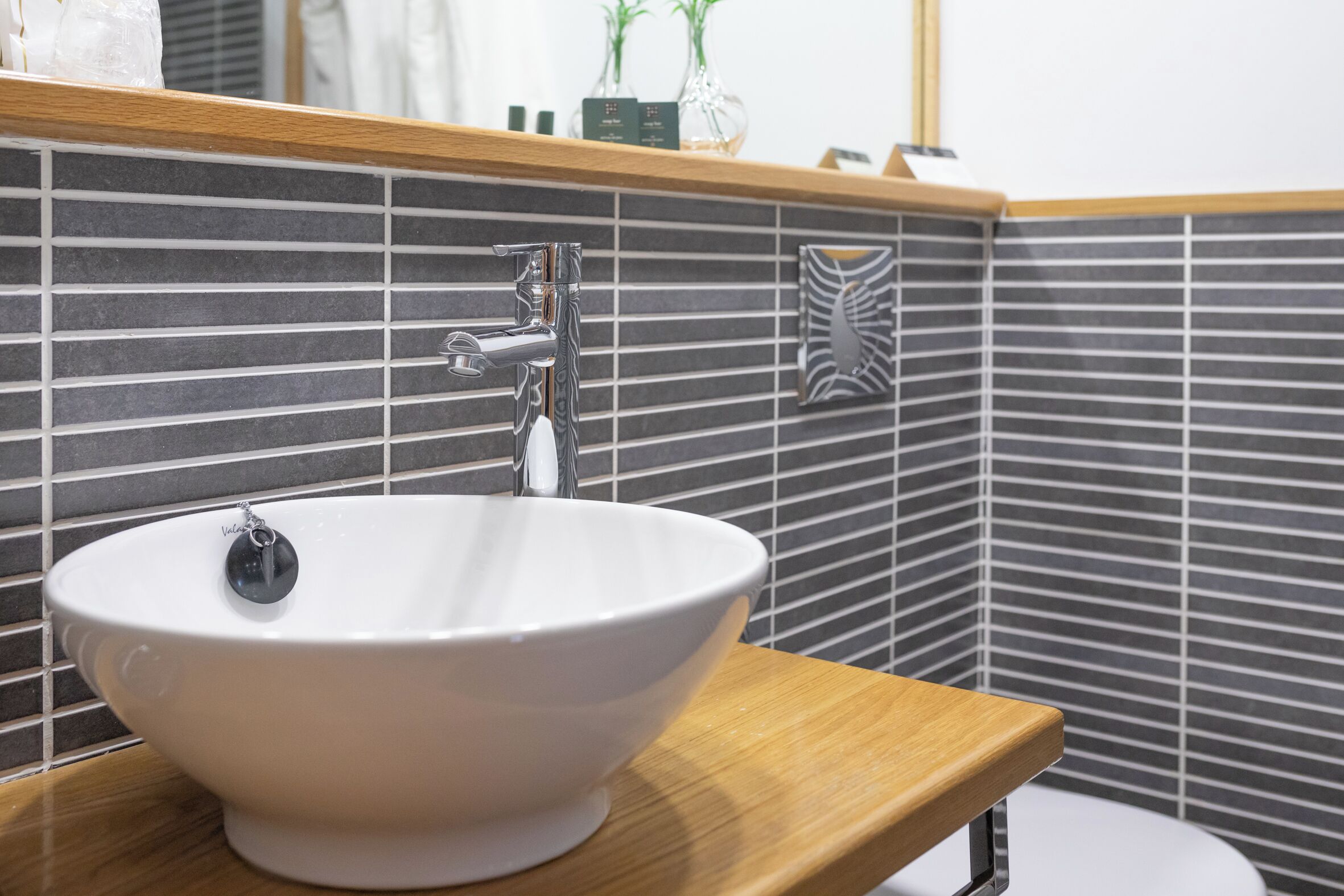 A white ceramic sink with a modern faucet on a wooden countertop in a bathroom with striped tile walls.