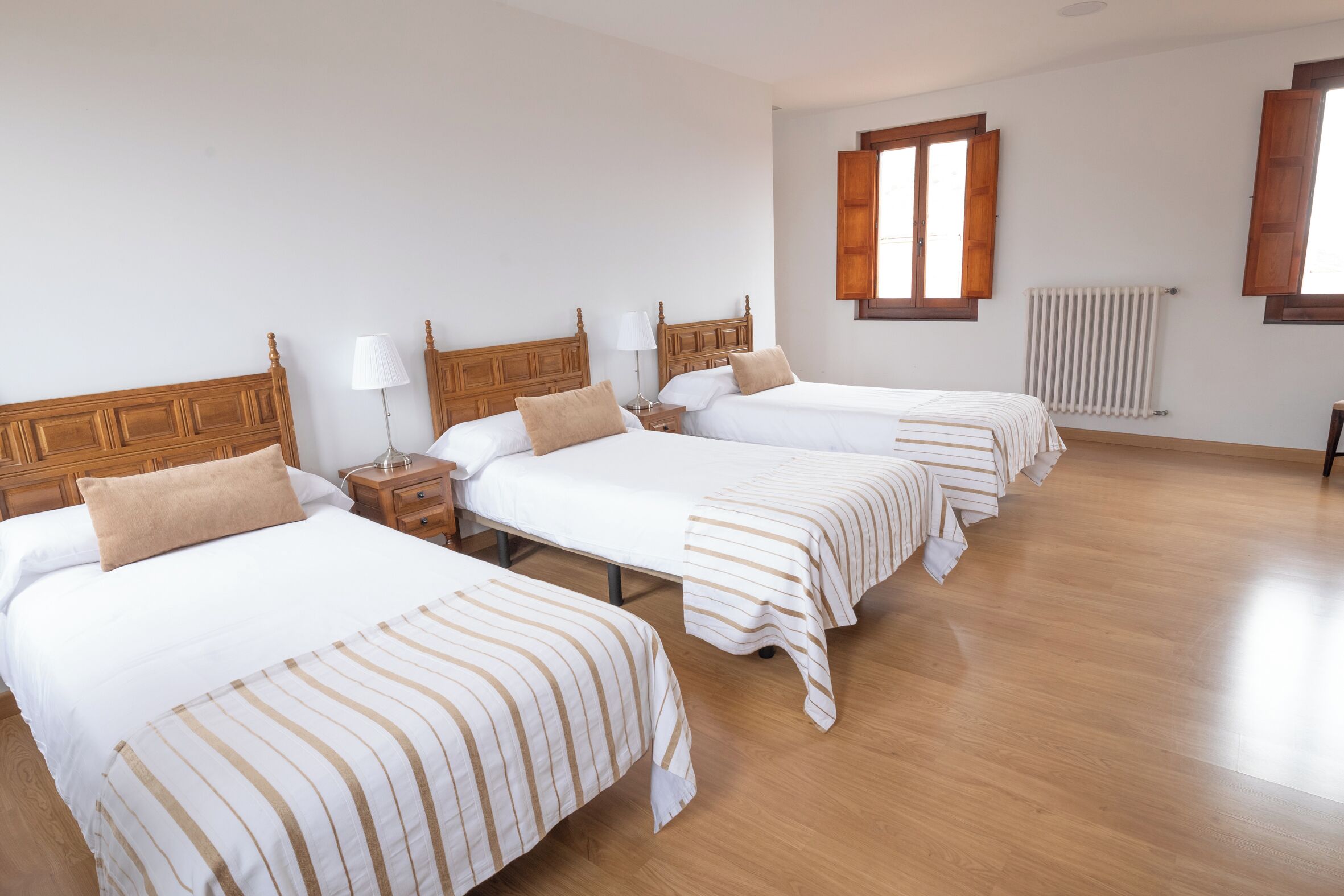 Una habitación de hotel con cuatro camas individuales, cabeceros de madera, ropa de cama blanca y piso de madera.