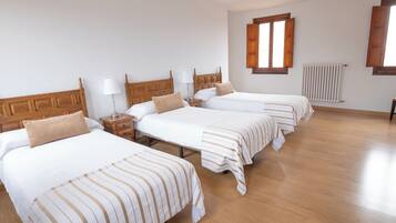 A hotel room with four single beds, wooden headboards, white bedding, and a wooden floor.