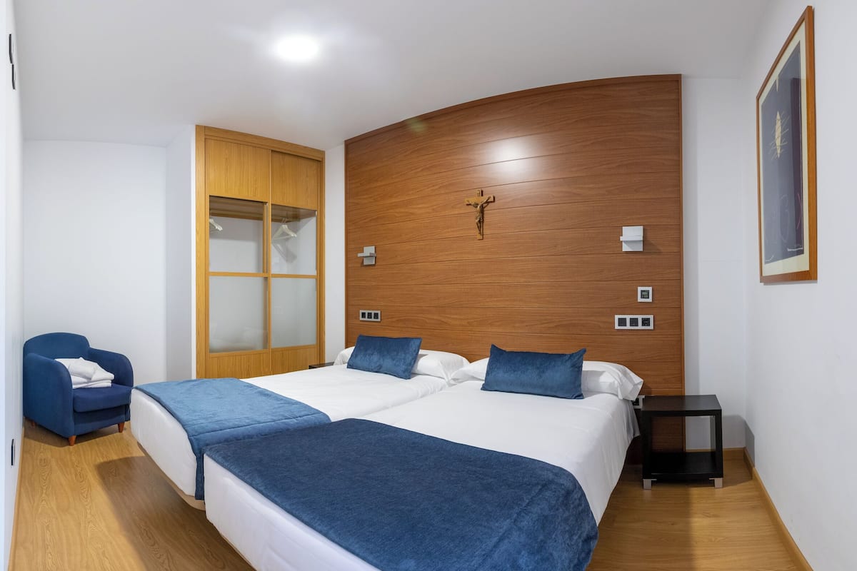 A bedroom with two beds, a wooden headboard, a blue chair, a nightstand, and a framed picture on the wall.