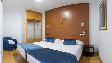 Un dormitorio con dos camas, cabecero de madera, una silla azul, una mesita de noche y un cuadro enmarcado en la pared.