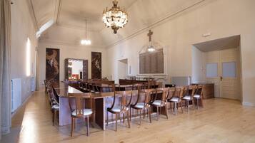 Un grand hall doté de tables et de chaises en bois, d’un lustre et d’une croix accrochée au mur.