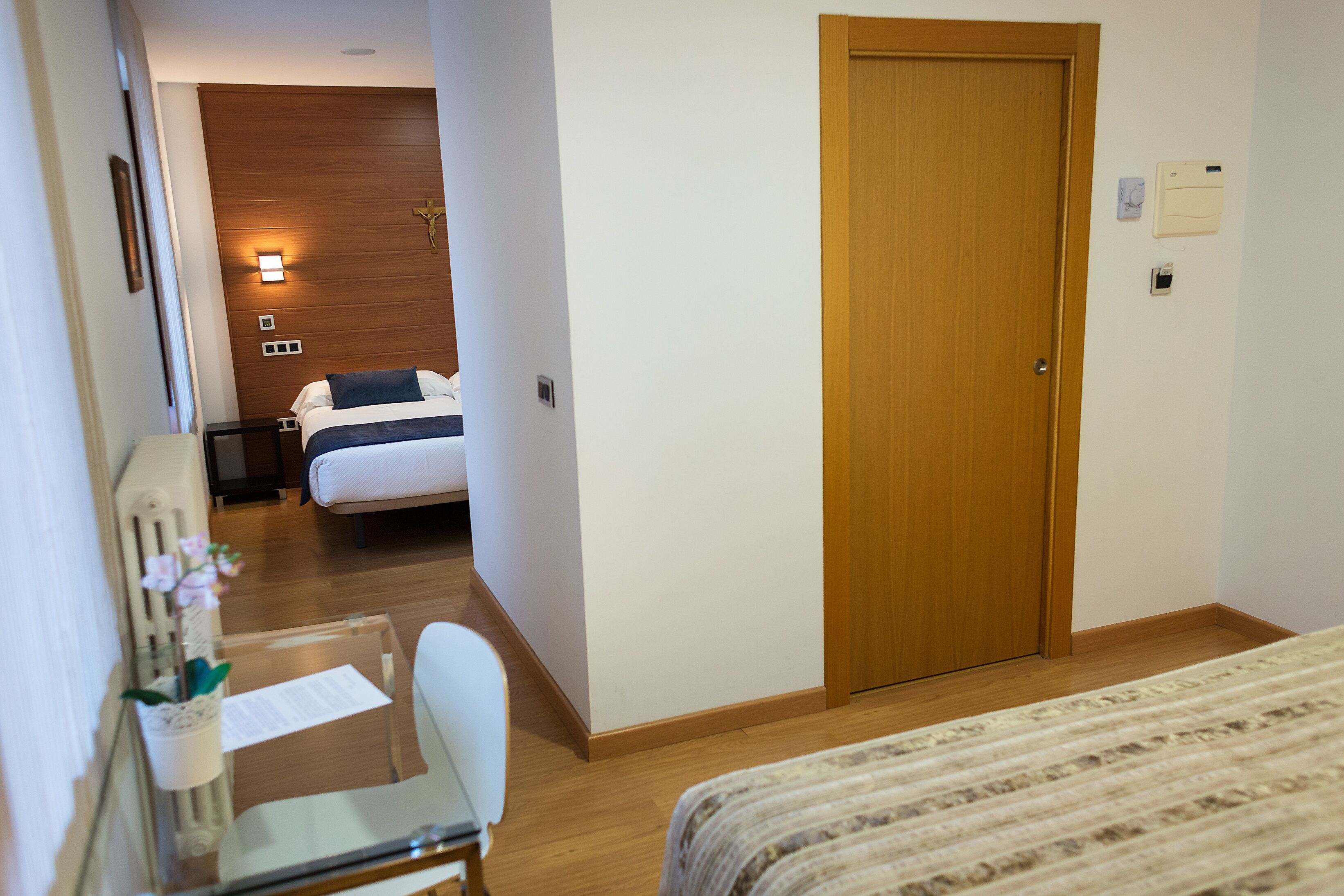 Habitación de hotel con puerta de madera, una cama con colcha a rayas, un escritorio con silla y una planta pequeña.