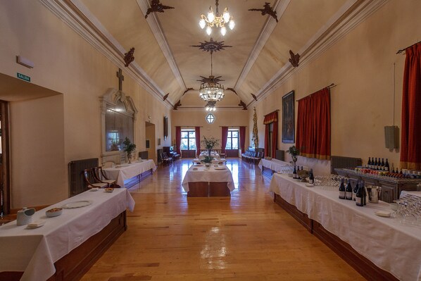 A long banquet hall with tables set for a meal, a chandelier, and a large window at the end. - Hospedería del Seminario (Cuenca)