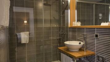 Un baño moderno con cabina de ducha de vidrio, tocador de madera con lavabo blanco y un espejo sobre el lavabo.