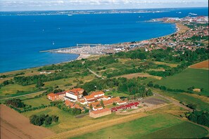 An aerial view of a coastal town with a marina, green fields, and a large building complex with red roofs. - Sundsgården hotell & konferens (Råå)