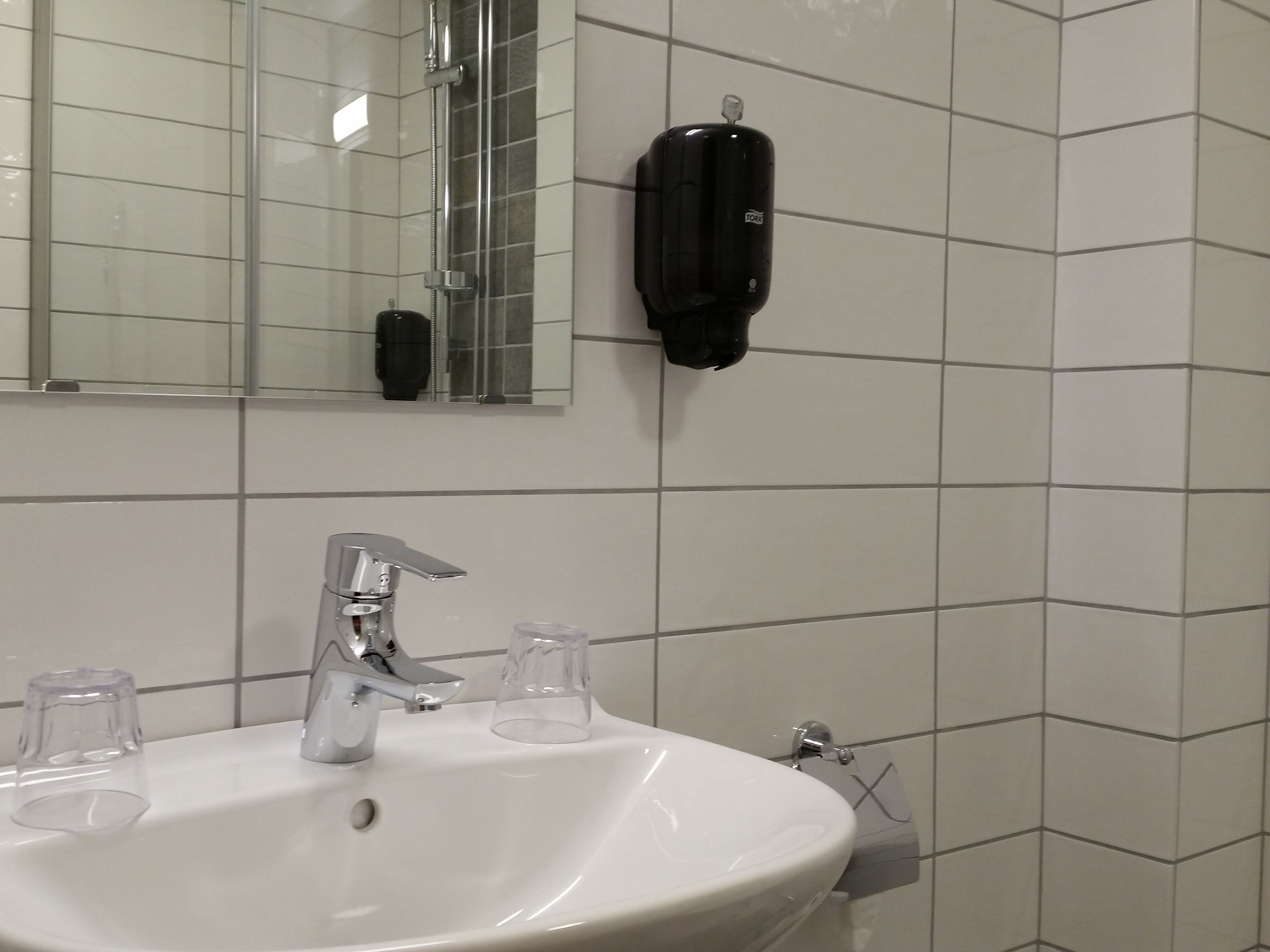A bathroom with a white sink, a mirror, and a black soap dispenser.