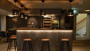 Een bar met een toonbank, krukken, hangende lampen en een koelkast vol flessen.